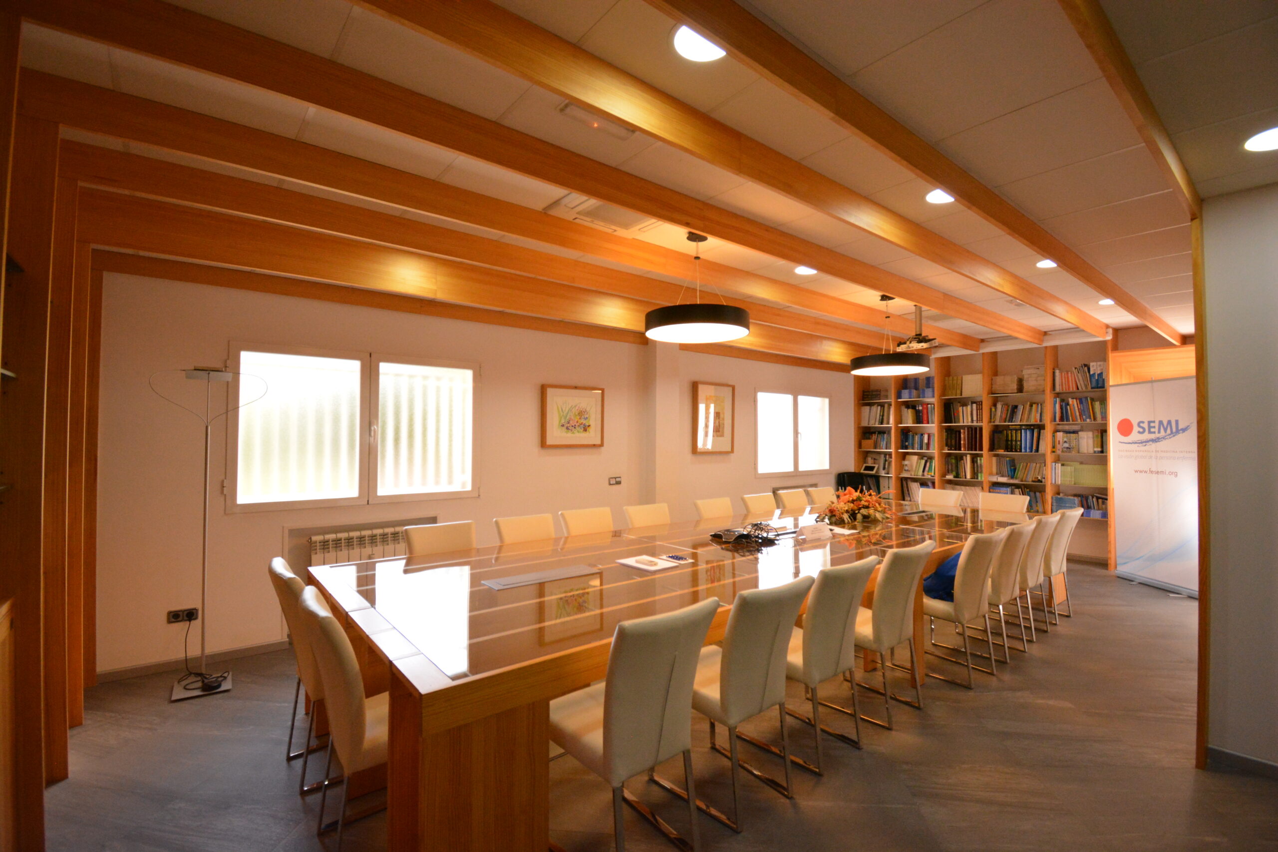 Espacio para reuniones 3 Sala de reuniones con una mesa central grande, rodeada de sillas blancas con detalles en madera.